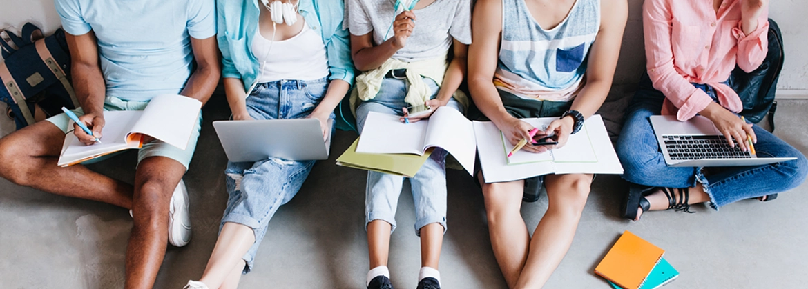 A group of students sitting together on steps with notebooks and laptops