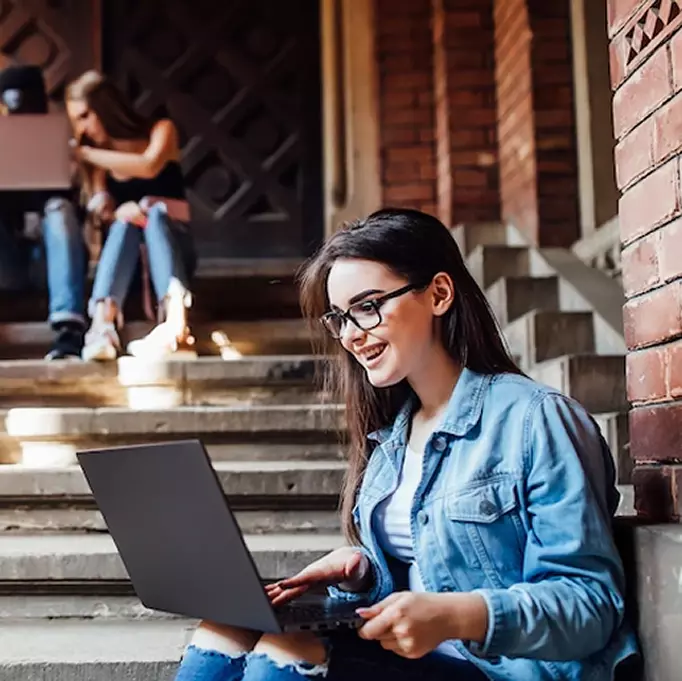 A student working on a laptop while sitting on outdoor steps