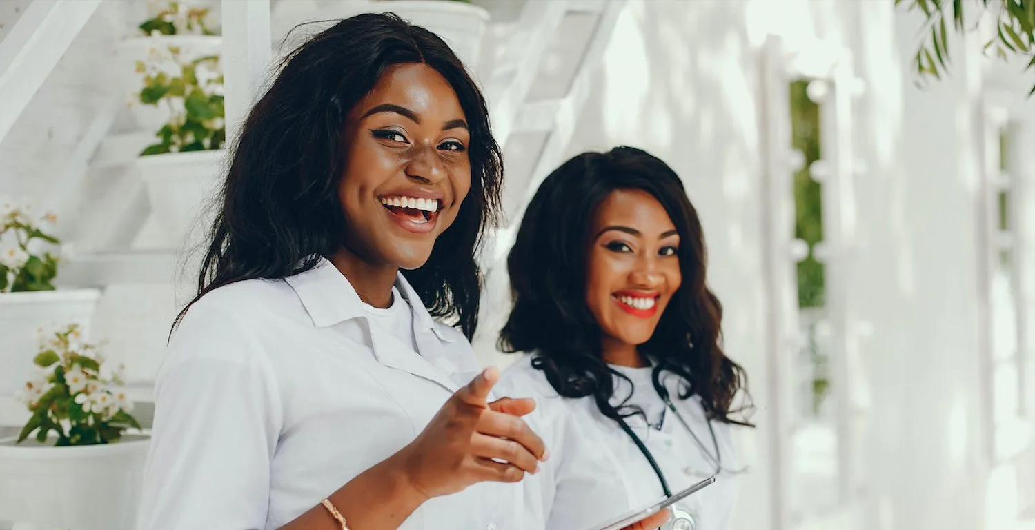 Two smiling medical students in white coats, one with a stethoscope