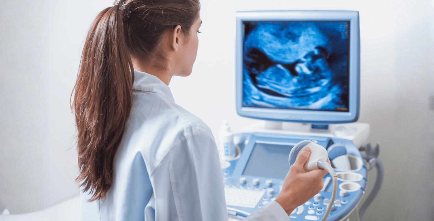 A sonographer holding an ultrasound probe while reading a scan on the monitor