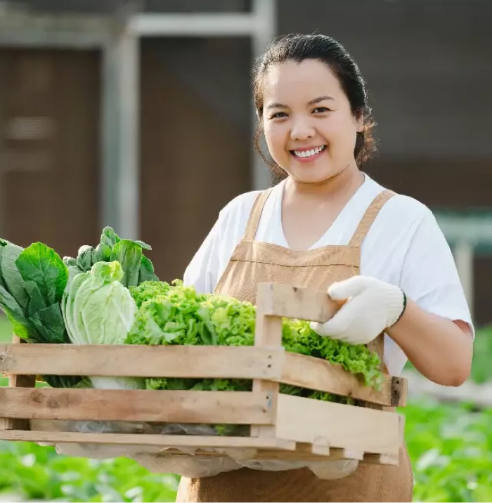 A smiling woman holding a wooden crate of fresh vegetables