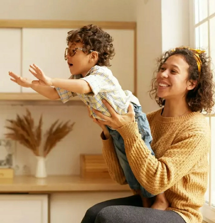 A young woman lifting a happy toddler in a bright kitchen