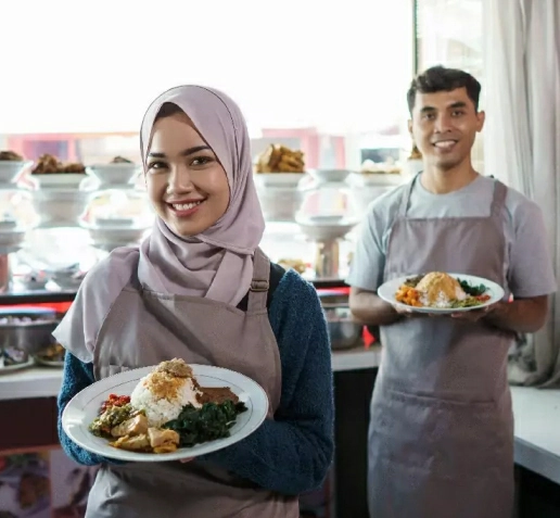 Two food service workers in aprons, one holding a plated meal