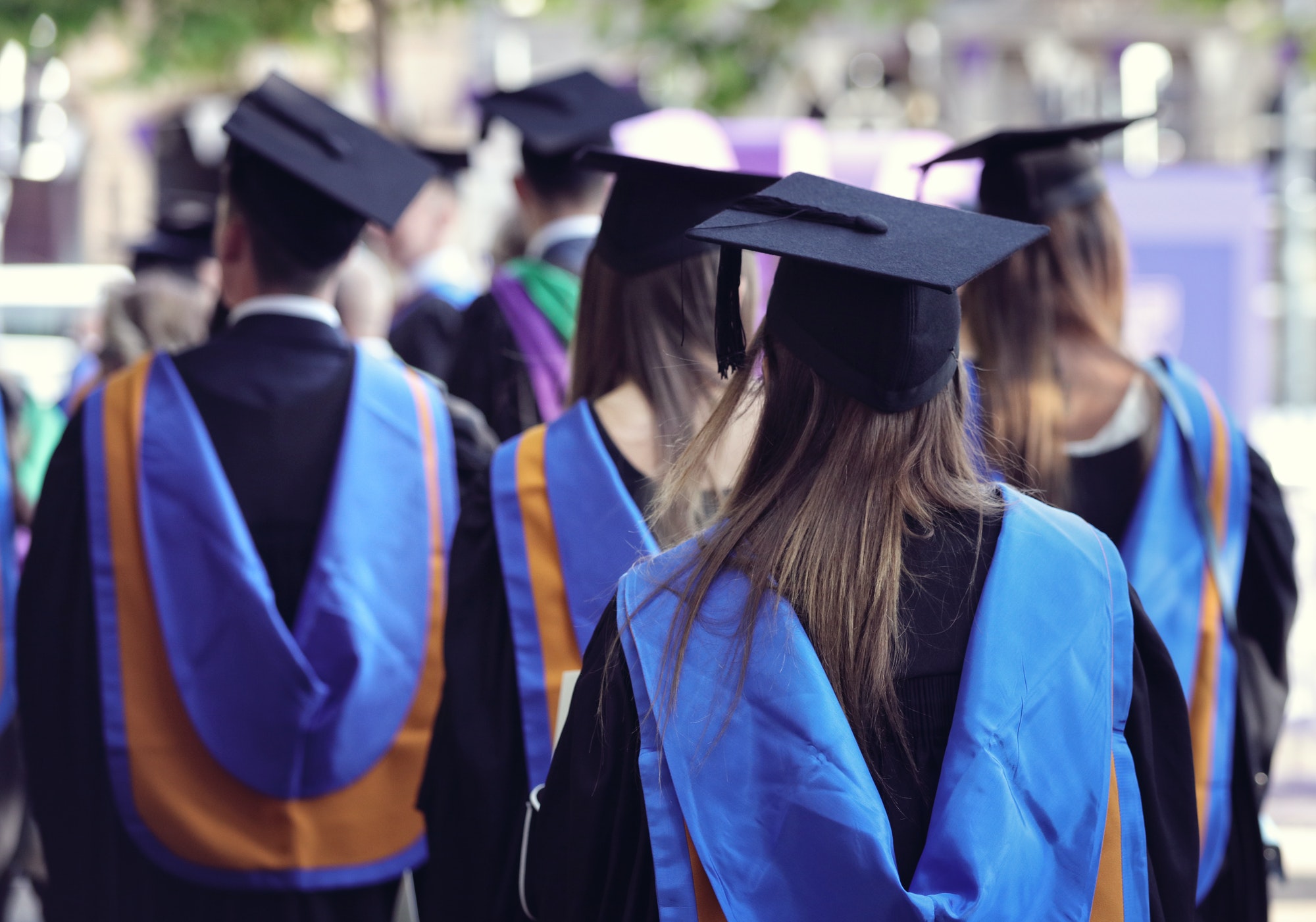 Graduates in caps and gowns with blue and gold hoods at a graduation ceremony