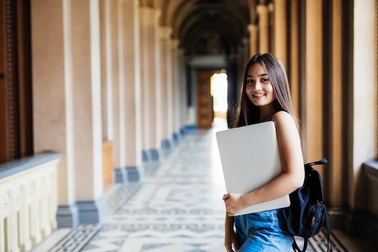 A student with a laptop walking through a university campus hallway